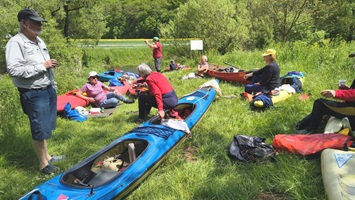 Gruppe von Personen in Kajaks während einer Mittagspause auf einer Wiese.