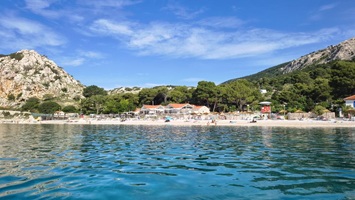 Blick auf einen Strand mit klarem Wasser, umgeben von Bäumen und Bergen.