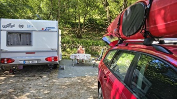 Ein Wohnwagen steht auf einem Campingplatz, während eine Person an einem Tisch im Freien sitzt.